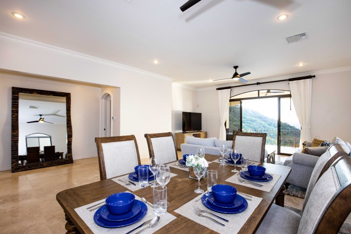 Bright dining and living area with blue tableware, large mirror, and mountain view through sliding doors.
