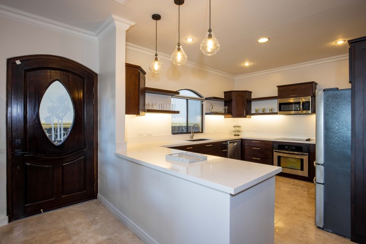 Modern kitchen with dark wood cabinets, island, stainless steel appliances, and pendant lights.