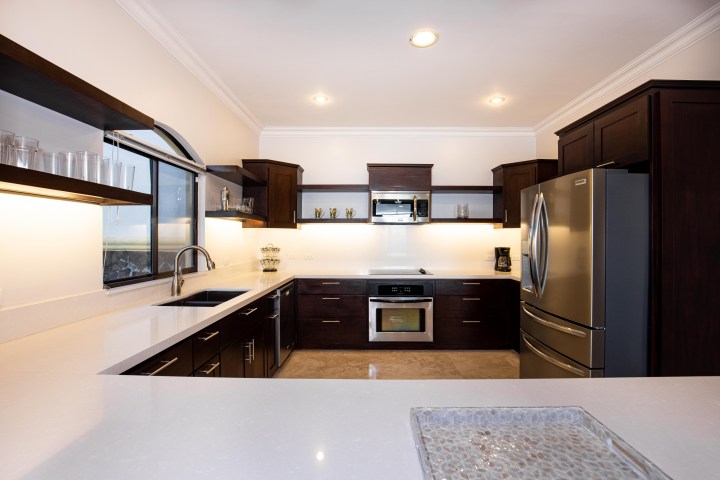 Modern kitchen with dark wood cabinets, stainless steel appliances, and white countertops.