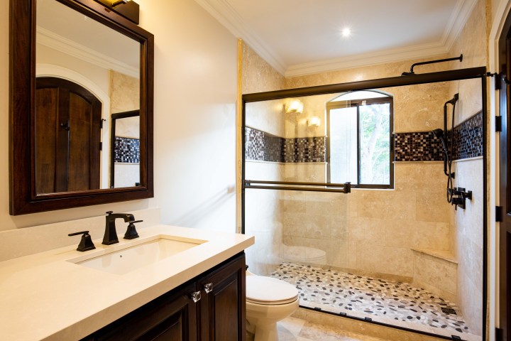 Elegant bathroom with glass shower, mosaic tiles, and dark wood vanity and mirror.
