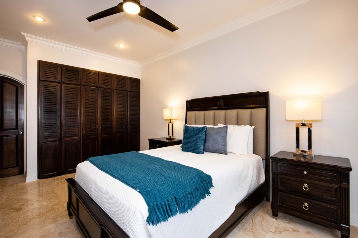 Modern bedroom with a queen bed, teal blanket, dark wood furniture, and soft lighting.