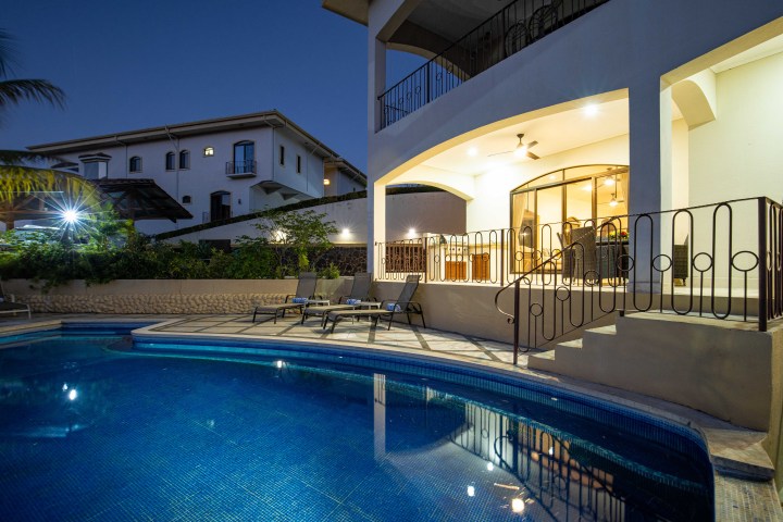 Night view of a villa with a lit pool and outdoor seating area.