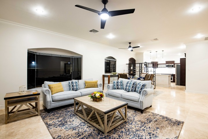 Modern living room with sofas, a coffee table, and ceiling fans, connected to a kitchen and dining area.