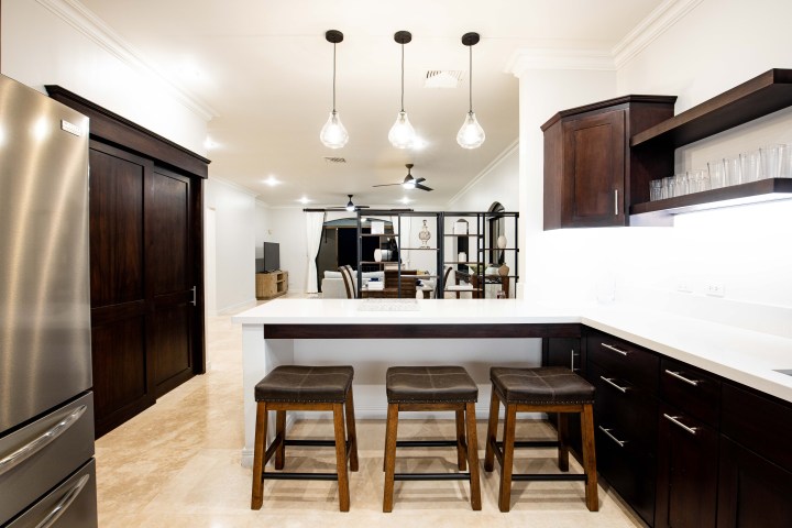 Modern kitchen with dark wood cabinets, a white countertop, and three pendant lights over stools.