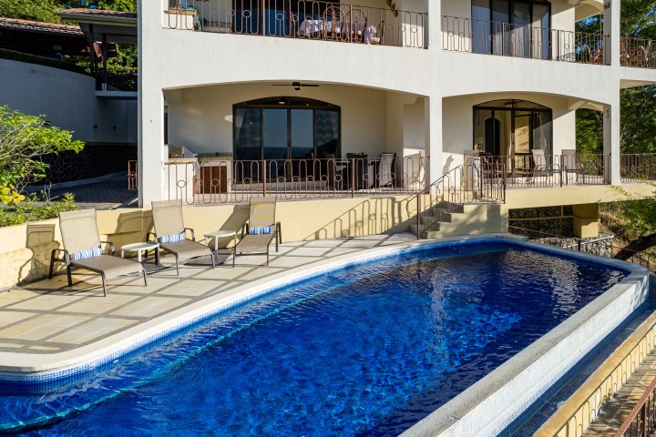 Outdoor pool with lounge chairs in front of a two-story building with balconies.