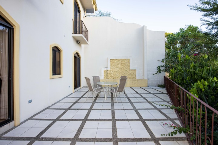 Outdoor patio with round table and chairs, tiled floor, and cream-colored building walls.