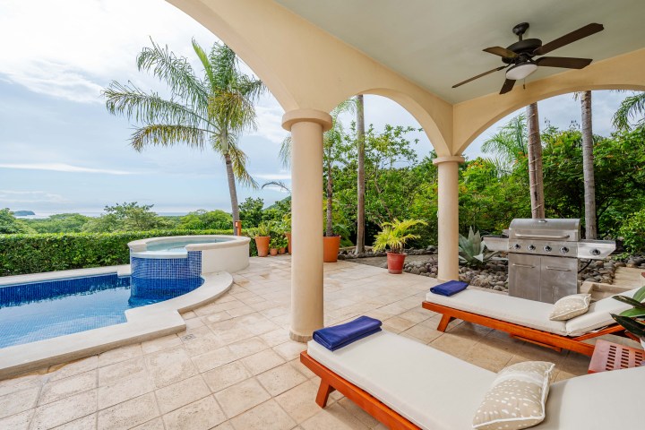 Outdoor patio with pool, jacuzzi, sun loungers, grill, and tropical view.