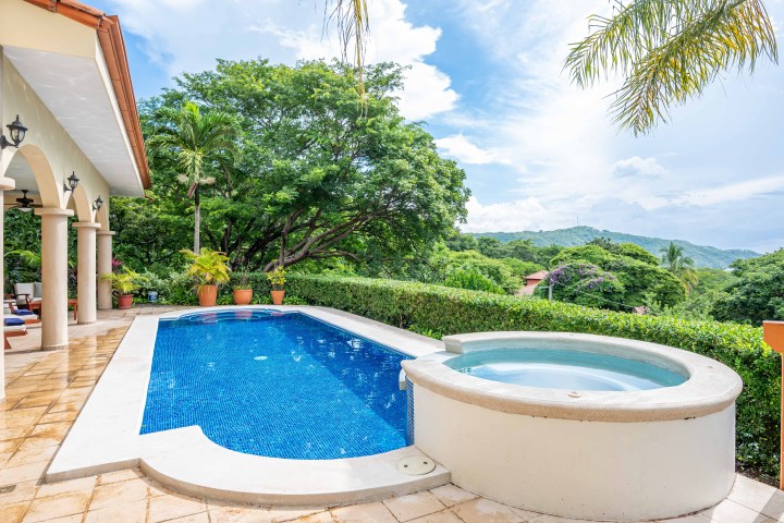 Outdoor pool and hot tub with mountain and lush greenery view.