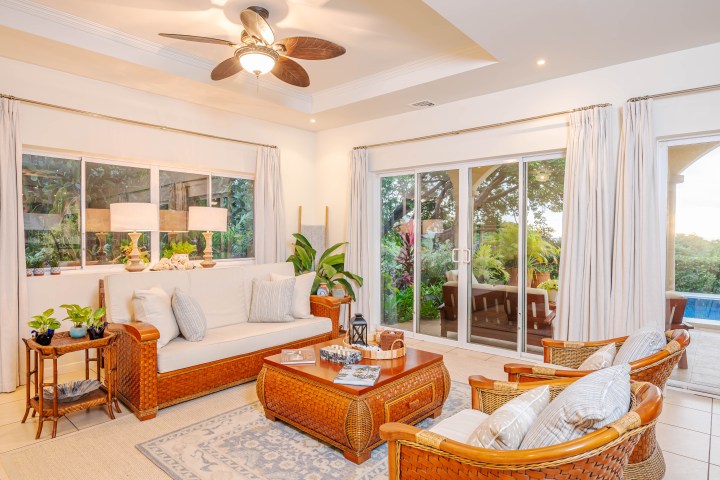 Bright living room with wicker furniture, ceiling fan, and large sliding glass doors leading to a garden.