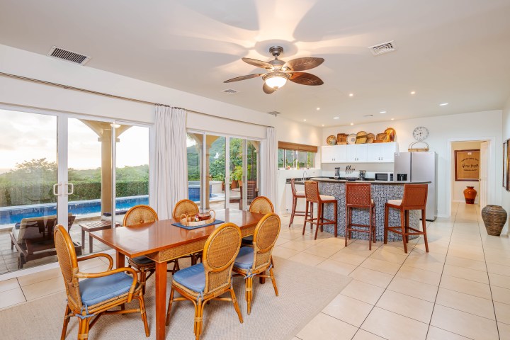 Open kitchen and dining area with wicker chairs and pool view through glass doors.