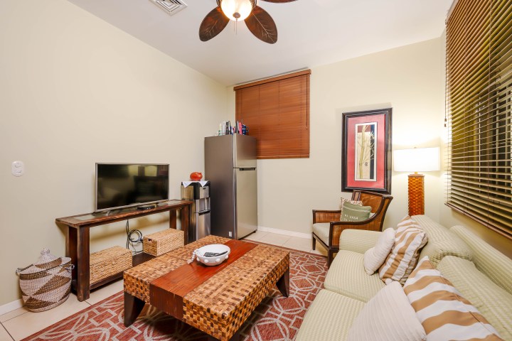 Cozy living room with sofa, TV, coffee table, and fridge, decorated with a ceiling fan and wall art.