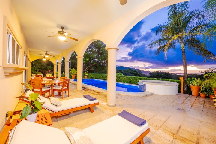 Outdoor patio with arches, pool, lounge chairs, and sunset view