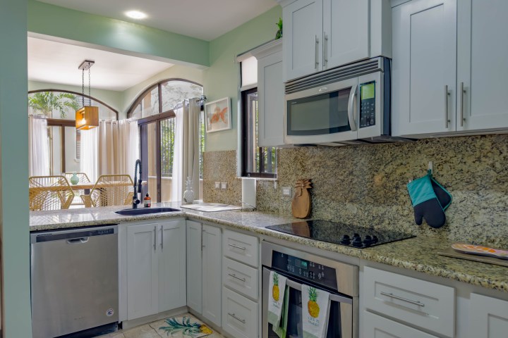 Modern kitchen with granite countertops, white cabinets, oven, microwave, and a view of a dining area with windows.
