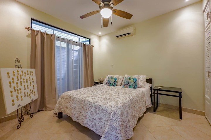 Bedroom with a bed, ceiling fan, side tables, and wall art under soft lighting.