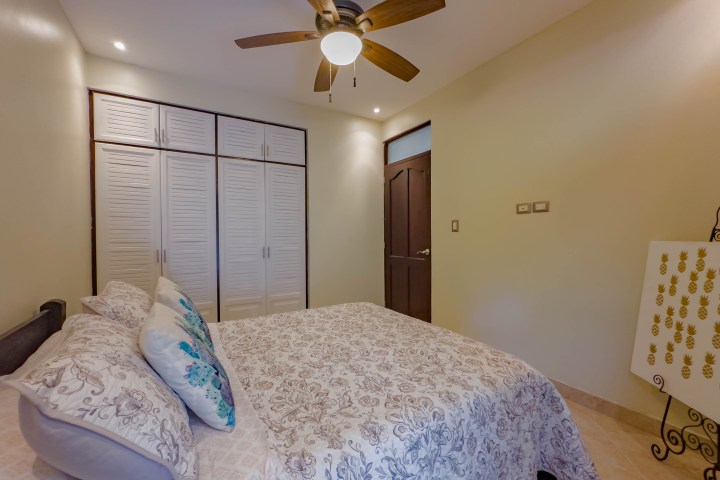 Bedroom with floral bedding, ceiling fan, and closet with louvered doors.