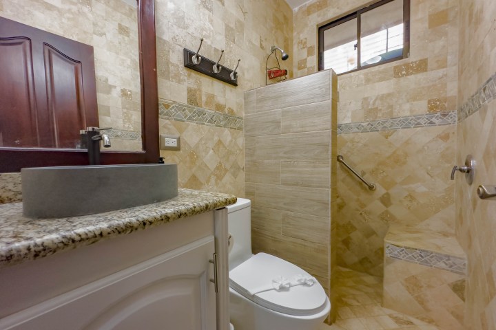 Bathroom with tiled walls, vessel sink, toilet, and open shower area.