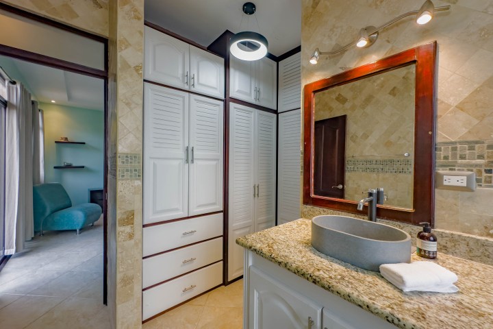 Bathroom with granite counter, mirror, round sink, and adjacent room with teal chair and shelves.
