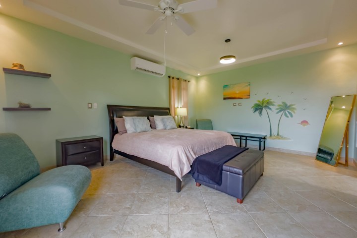 Bedroom with a green accent wall, double bed, seating, wall art, and mirror.