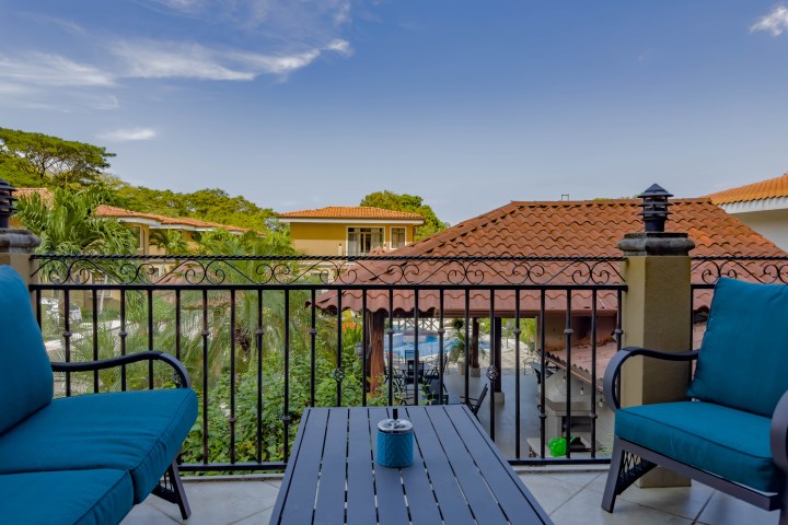 Balcony with blue chairs, table, and view of tiled roofs and greenery.