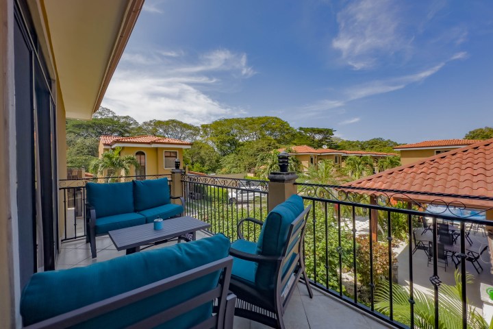 Balcony with teal cushions overlooking courtyard with tiled roofs and greenery.