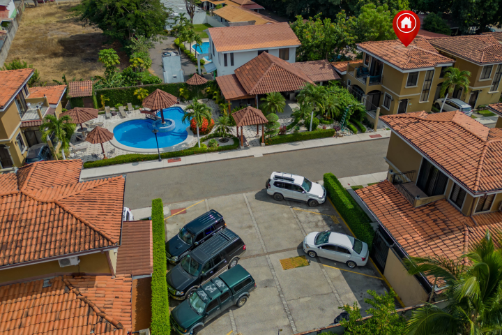 Aerial view of a residential area with houses, a pool, and parked cars.