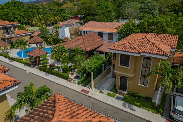 Aerial view of a tropical residential area with orange-roofed houses, a pool, and greenery.