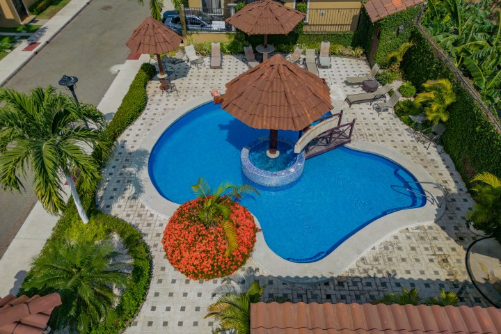 Aerial view of a residential pool area with umbrellas and seating surrounded by palm trees.