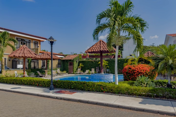Tropical courtyard with palm trees, a gazebo, and a small pool surrounded by colorful plants and shrubbery.
