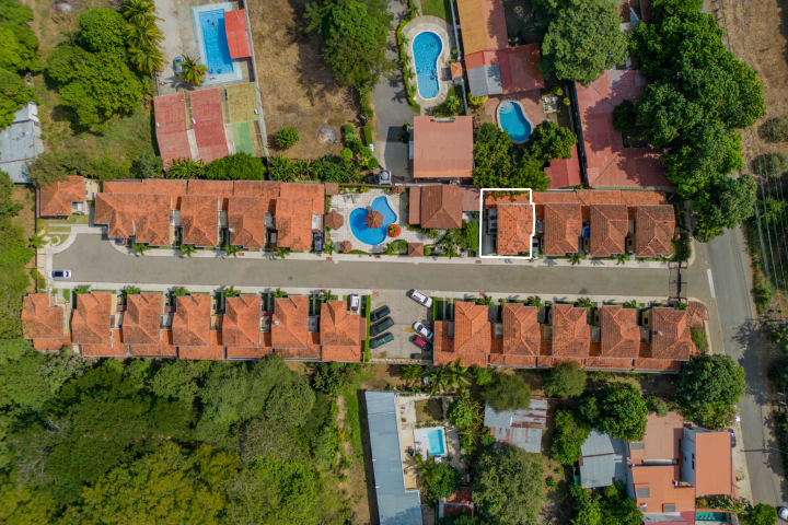 Aerial view of housing complex with red roofs, pools, and cars on streets lined with trees.