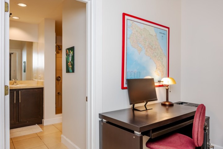 Small desk with computer, map on wall, and an open door leading to a bathroom.