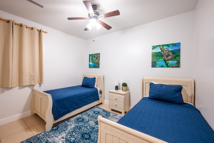 Bedroom with two single beds, blue bedding, artwork of sloths, and a ceiling fan.