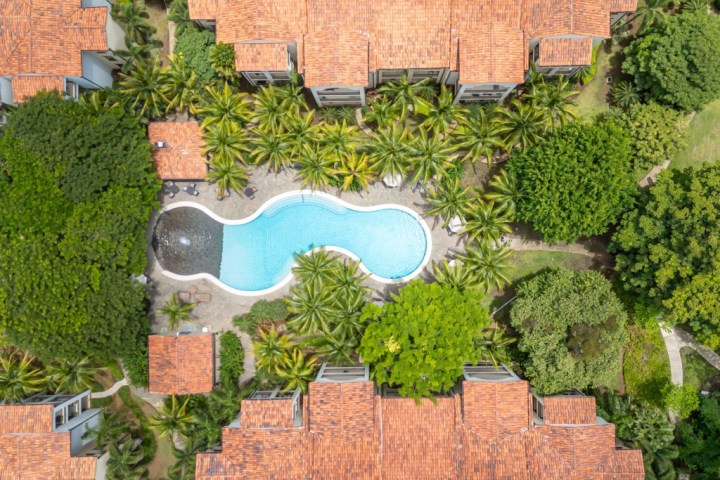 Aerial view of a curvy pool surrounded by trees and buildings with red roofs.