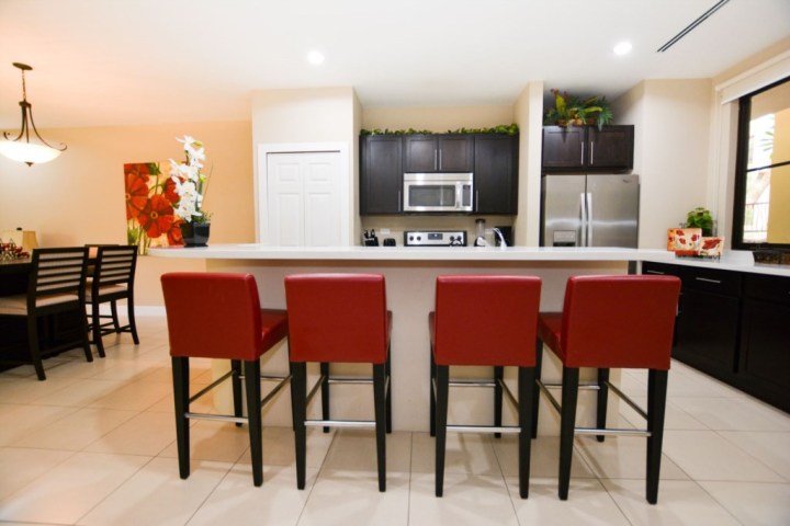Modern kitchen with red bar stools, dark cabinets, and stainless steel appliances.