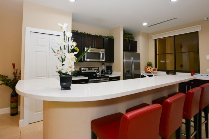 Modern kitchen with red chairs, a white island, and stainless steel appliances.