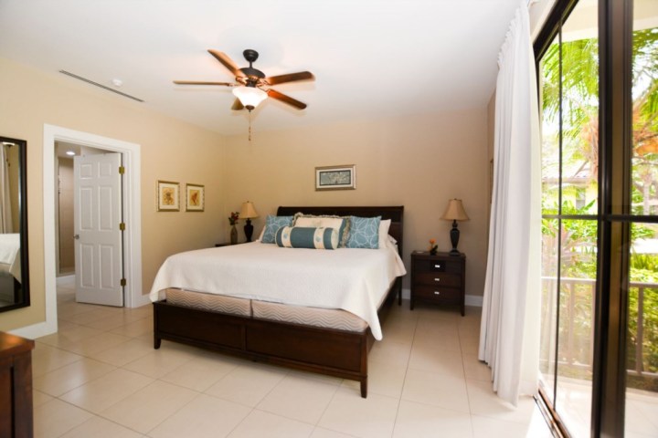 Bright bedroom with king bed, ceiling fan, two nightstands, and glass door to balcony.