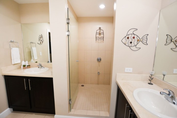 Bathroom with two sinks, a glass shower, and fish wall art on beige walls.
