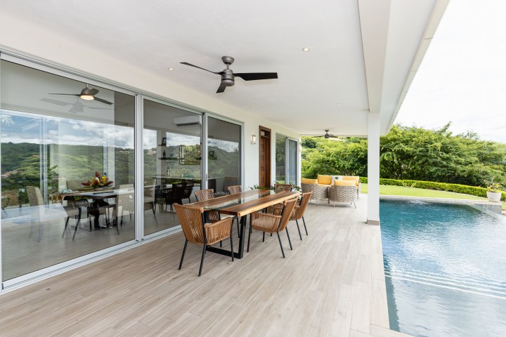 Outdoor patio with dining table, ceiling fan, pool, and view of green landscape.