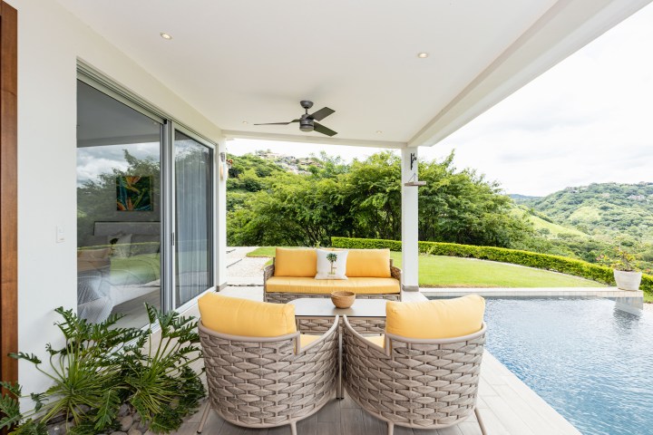 Outdoor patio with yellow-cushioned seating, pool, and scenic green hillside view.