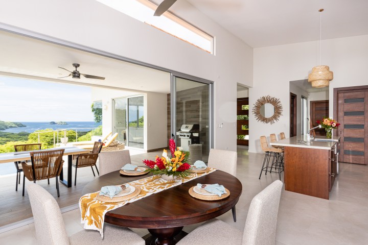Modern open-plan dining area with ocean view, large windows, kitchen island, and outdoor seating.