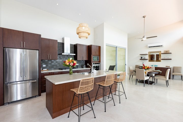 Modern kitchen with dark wood cabinets, island, bar stools, and dining area with beige chairs.