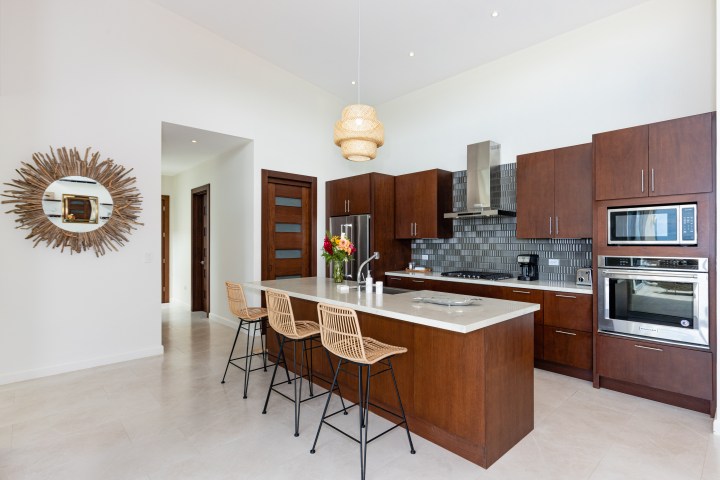 Modern kitchen with wood cabinets, island, wicker stools, and circular mirror on wall.