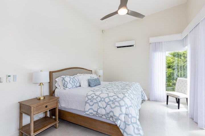 Bright bedroom with bed, side table, chair, window, and ceiling fan.