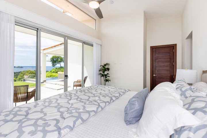 Bright bedroom with ocean view, sliding doors, and patterned bedding.