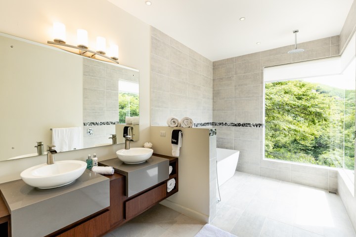 Modern bathroom with dual sinks, large mirror, bathtub, and scenic window view.