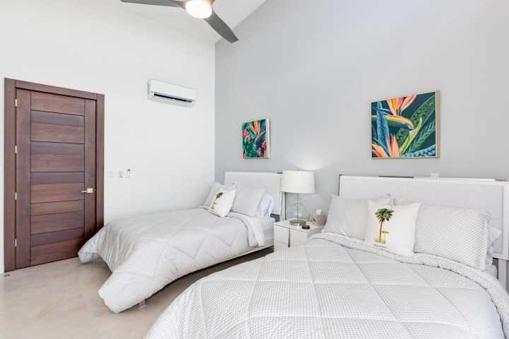 Bedroom with two beds, wooden door, white walls, and tropical wall art.
