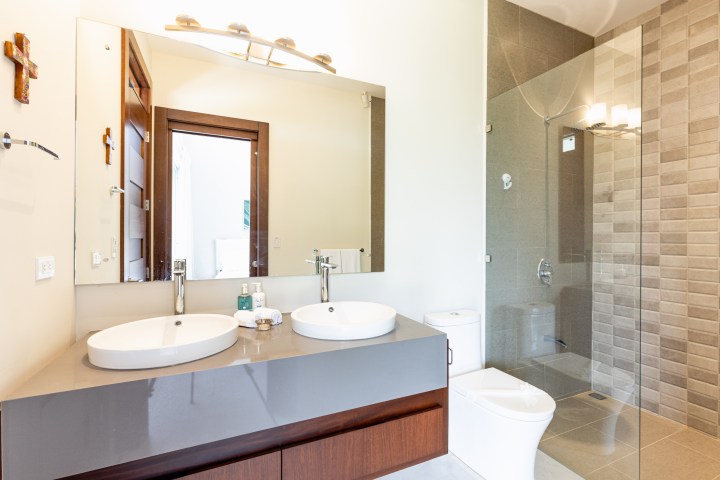 Modern bathroom with double sinks, large mirror, and glass shower enclosure.