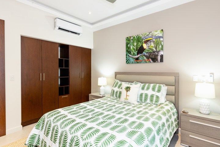 Bedroom with tropical-themed bedding, wardrobe, and lamps, under a nature painting.