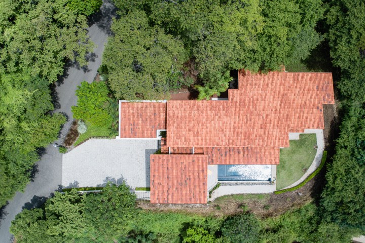 Aerial view of a red-roofed house surrounded by dense green trees and a driveway.