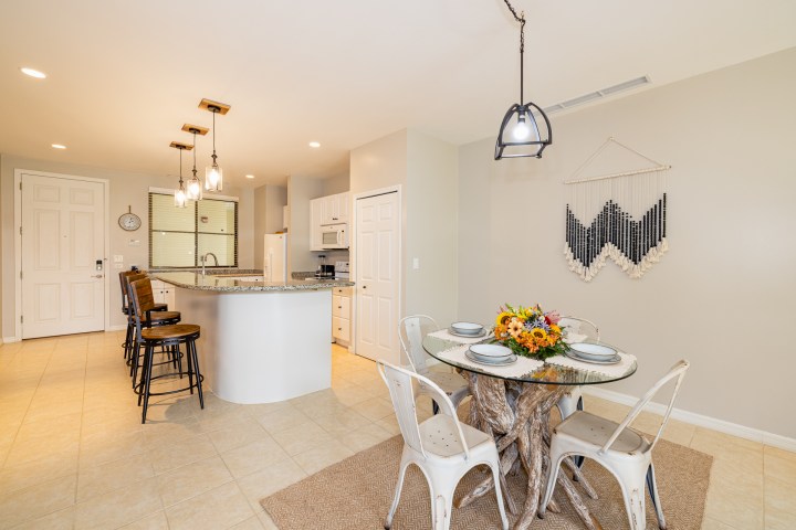 Modern kitchen with island, bar stools, and dining table with floral centerpiece in a neutral-toned room.