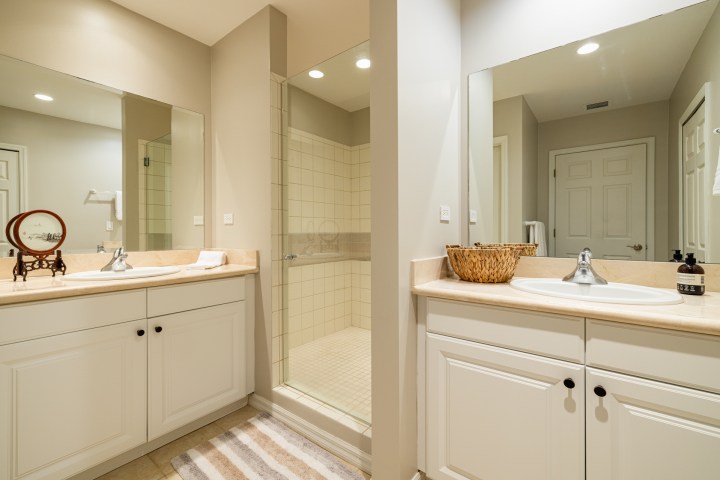White bathroom with dual sinks, mirrors, walk-in shower, and striped rug.